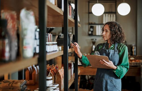 Mature Deli Owner Taking Inventory On Store Shelves Using A Clipboard
